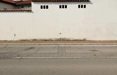 White plaster wall with roof tiles on top at the roadside. Porphyry sidewalk and street in front. Background for copy space.