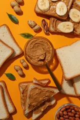  Peanut paste in a jar with sandwiches next to it on a yellow background. © Atlas