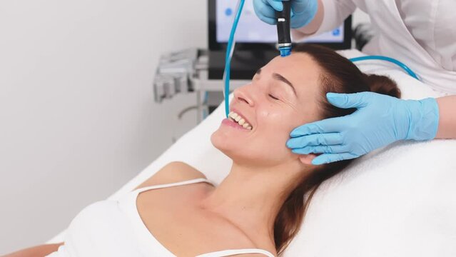A cosmetologist wearing gloves performs vacuum cleaning and polishing of the facial skin of a middle-aged woman in a cosmetology clinic. Professional moisturizing and rejuvenating hardware procedures.