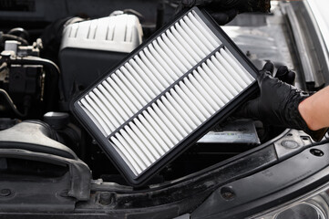 Auto mechanic holds car air filter in his hands near engine compartment, close-up. Concept of...