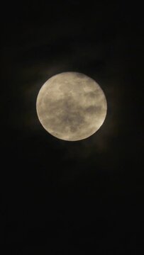 Full Moon in the dark night sky with black flying clouds. Real shooting through a telephoto lens