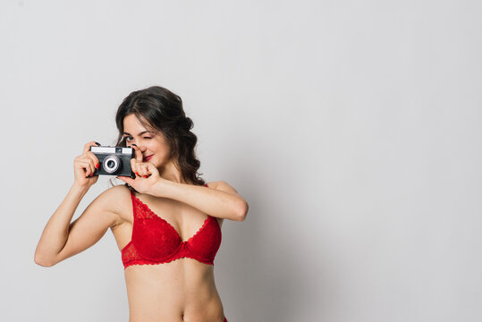 Beautiful female with pretty smile in red lingerie holding photo camera, isolated on white