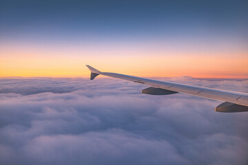 Airplane flying over color sky clouds during scenic sunset or sunrise cloudscape, view from plane window of wing turbines and horizon