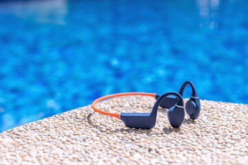 Colorful orange and navy blue bone conduction headphones lie by the poolside, basking in the summer...