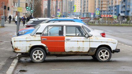 An old white rusty Soviet car with a red door is parked on the street, Soyuzny Prospekt, St....