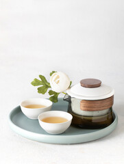 Asian tea modern ceremony set with crystal pot and ceramic bowl cup with green tea on a try with white flowers - 782910681