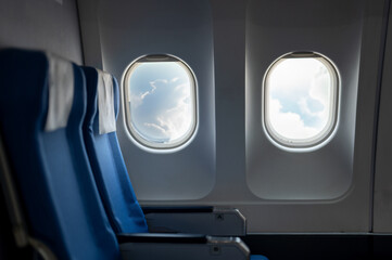 The calming scene of empty blue airplane seats beside a window showcasing a view of the sky and clouds, invoking a sense of peaceful travel.