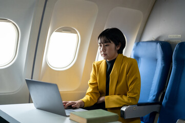 Smiling businesswoman in a yellow blazer using a laptop on a tray table, working efficiently on an airplane.
