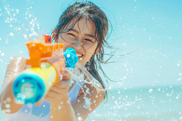 Happy traveler asian woman wearing summer shirt holding colorful squirt water gun over blur sea, Water festival holiday concept