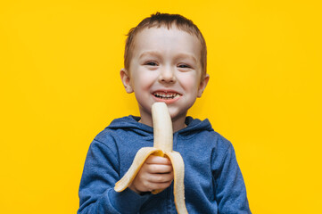 A small funny cheerful ukrainian boy bites a banana, makes faces and plays around. Studio...