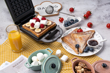 Golden Waffle Maker with Banana and Strawberries Breakfast Spread on Gingham Table, Vibrant Morning Scene Featuring Blueberry Jam, Cotton Candy and Fresh Orange Juice
