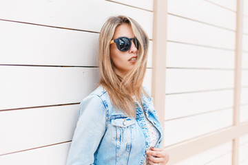 Fashionable beautiful teenager girl with vintage style sunglasses in a fashion denim jacket and...