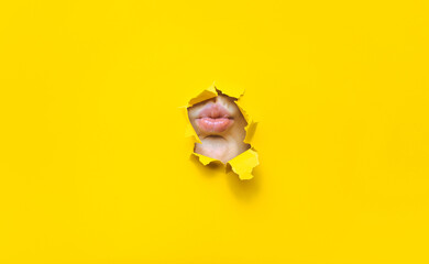 A child's lips appear in a torn hole of yellow paper. Imitation of a kiss. Silence concept. - obrazy, fototapety, plakaty