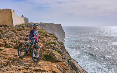 happy active senior woman cycling during moody golden hour near sunset at the the rock cliffs and...