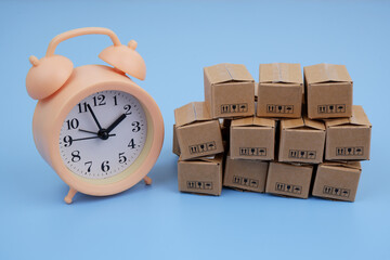 Shipping and storage time concept. Alarm clock and carton boxes on blue background.	