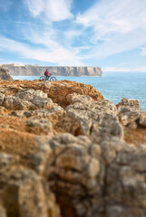 happy active senior woman cycling at the the rock cliffs and lighthouse of Cabo Sao Vicente, the south-western spit of Europe at the atlantic coast of Algarve, Portugal, 