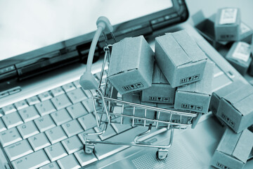 Shopping trolley and many carton boxes on laptop computer keyboard. Online purchase concept.	