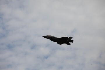 Side view of a fighter jet flying in blue cloudy sky