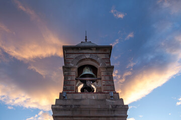 Stone belfry with bronze bell at the top of Lycabettus mount, Athens, during a glorious sunset with colorful clouds. 