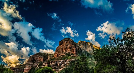 Low-angle shot of mesmerizing rocky mountains, green plants on slopes under a blue sky