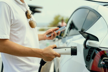 Hand insert EV charger plug into electric vehicle to recharge EV car, battery status display on...