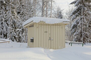 Old toilet (WC) made of wood in forest in winter with snow covering the ground.