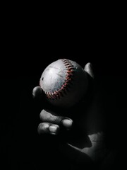 Hand holding a baseball ball in darkness