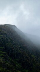 Vertical shot of a rocky mountain slope on a cloudy and misty day