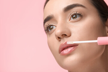 Woman applying lip gloss on pink background, space for text