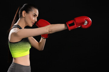 Beautiful woman in boxing gloves training on black background