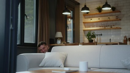 Young funny man looking at camera having fun alone doing prank illusion of disappearance pretending go down stairs at home