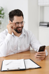 Handsome young man using smartphone at wooden table in office