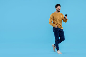 Happy young man using smartphone on light blue background, space for text - Powered by Adobe