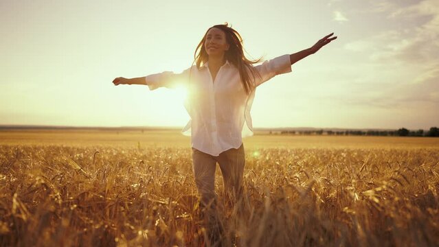 Romantic carefree happy woman running on yellow wheat field with spreading flying arms enjoying freedom calmness on rural nature during vacations holidays. Rest, relax lifestyle, village at sunset.