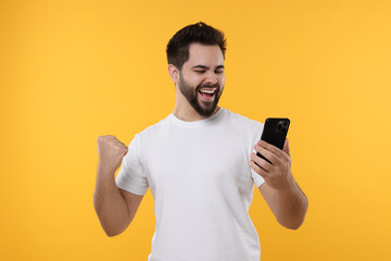 Happy young man using smartphone on yellow background