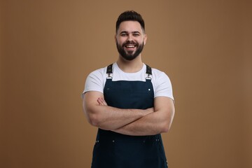 Smiling man in kitchen apron with crossed arms on brown background. Mockup for design