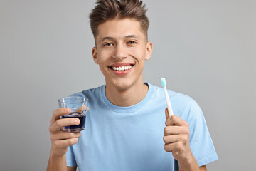 Young man with mouthwash and toothbrush on light grey background