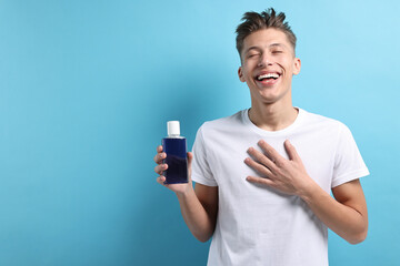 Young man with mouthwash on light blue background, space for text