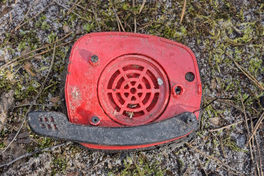 large broken headphones with one red plastic speaker and a black microphone lies on green moss and ground on the street