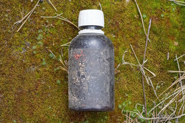 one small closed glass brown medical bottle with a white cap lies on green moss in nature