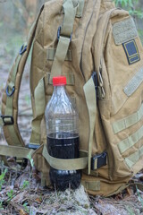 Fototapeta premium one full brown army backpack and a plastic bottle with a black drink in the pocket stand on the ground on the street