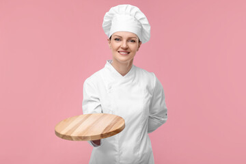 Happy chef in uniform holding empty wooden board on pink background