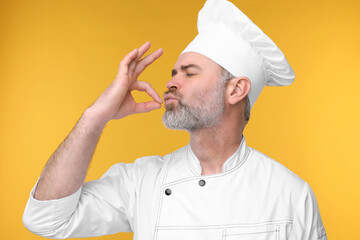 Chef in uniform showing perfect sign on orange background