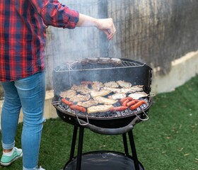 Shot of a person making barbecue on a grill in a green backyard