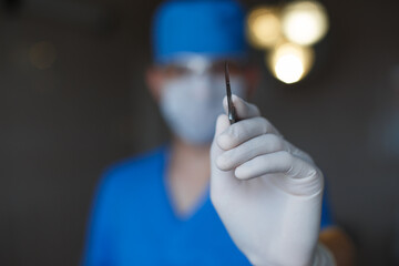 Doctor surgeon in a blue uniform holds a scalpel and performs an operation, close-up - obrazy, fototapety, plakaty