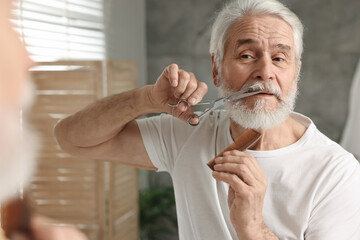 Senior man trimming mustache with scissors near mirror in bathroom