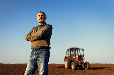 Portrait of satisfied mature farmer standing in field preparing to cultivate the land with a...