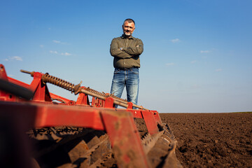 Portrait of satisfied mature farmer standing in field preparing to cultivate the land with a...