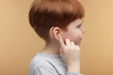 Little boy with hearing aid on pale brown background