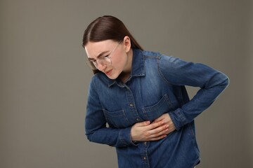 Woman suffering from stomach pain on grey background, space for text